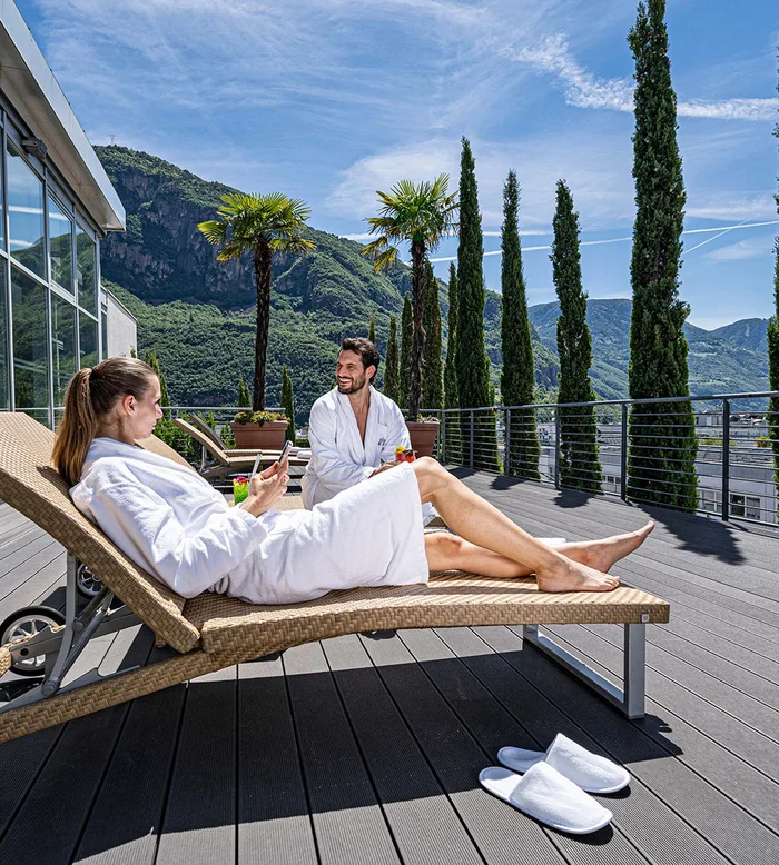 Coppia rilassante in accappatoi su terrazza con vista montagna e cipressi