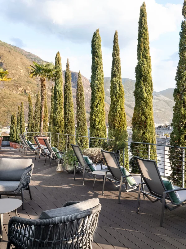 Terrasse mit Stühlen und hohen Bäumen neben einem Berg