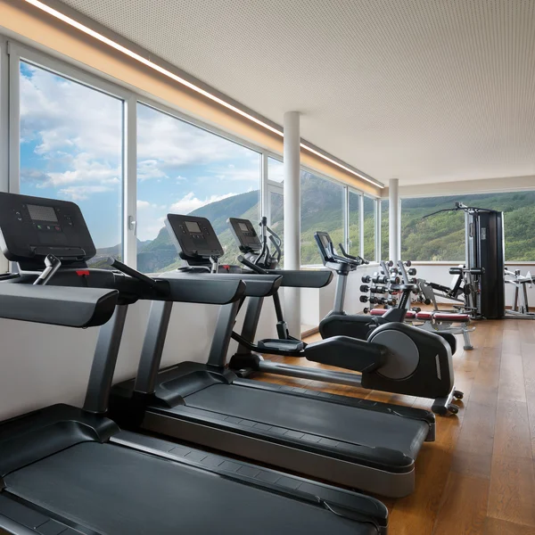 Modern gym with equipment near large windows overlooking mountains