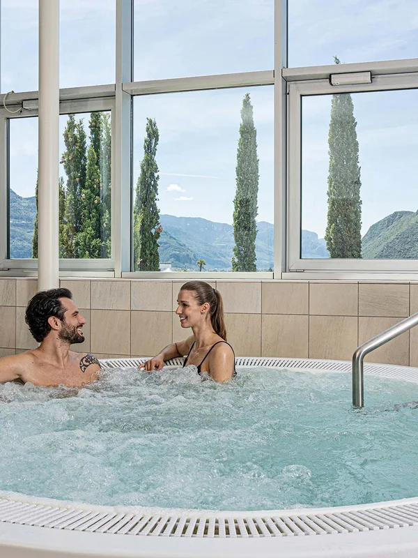 Entspanntes Paar im Whirlpool mit Bergblick durch große Fenster