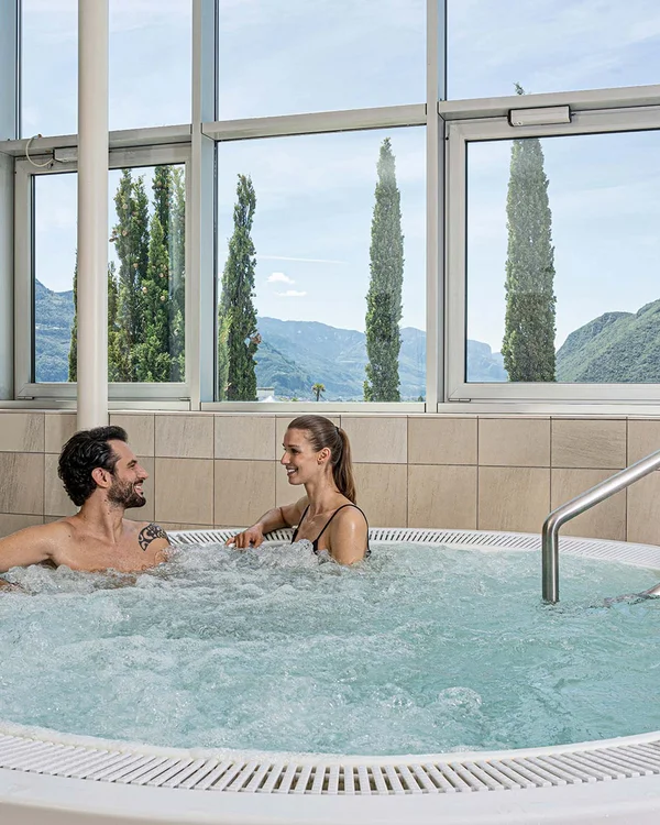 Relaxed couple in hot tub with mountain view through large windows